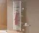 Vertikaler Kermi-Heizkörper in Weiß mit gerillter Oberfläche, montiert an einer Wand, mit einem pinken Handtuch und einem Beistelltisch im Vordergrund.