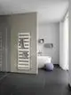 Weißer Kermi-Heizkörper mit horizontalen Längsrippen an einer hellen Wand, neben einer Duschkabine, mit Handtüchern und einem modernen Badbereich im Hintergrund.