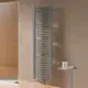 Kermi-Heizkörper, vertikal montiert, gerippte Oberfläche in graphit vor einer hellen Wand, neben einem kleinen Tisch mit Pflegeprodukten. Dusche im Hintergrund.