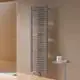 Vertikaler Kermi-Badheizkörper in mattem Bronze-Finish, mit horizontalen Röhren montiert an einer beige Wand, neben einem kleinen Tisch mit Pflegeprodukten.