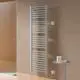 Vertikaler Kermi-Heizkörper in Silber, montiert an einer Wand, mit gestapelten Rohren, daneben ein kleiner Tisch mit Pflegeprodukten.