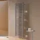 Vertikaler Kermi-Heizkörper in mattbronze mit Längsrippen, montiert an einer hellen Wand neben einem runden Tisch mit Pflegeprodukten. Dusche im Hintergrund sichtbar.
