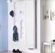Purmo-Heizkörper, vertikal montiert, mit gerillter Oberfläche an heller Wand. Jacke, Hut und Schuhe sind im Raum sichtbar. Wandhaken in Baumäste-Design.