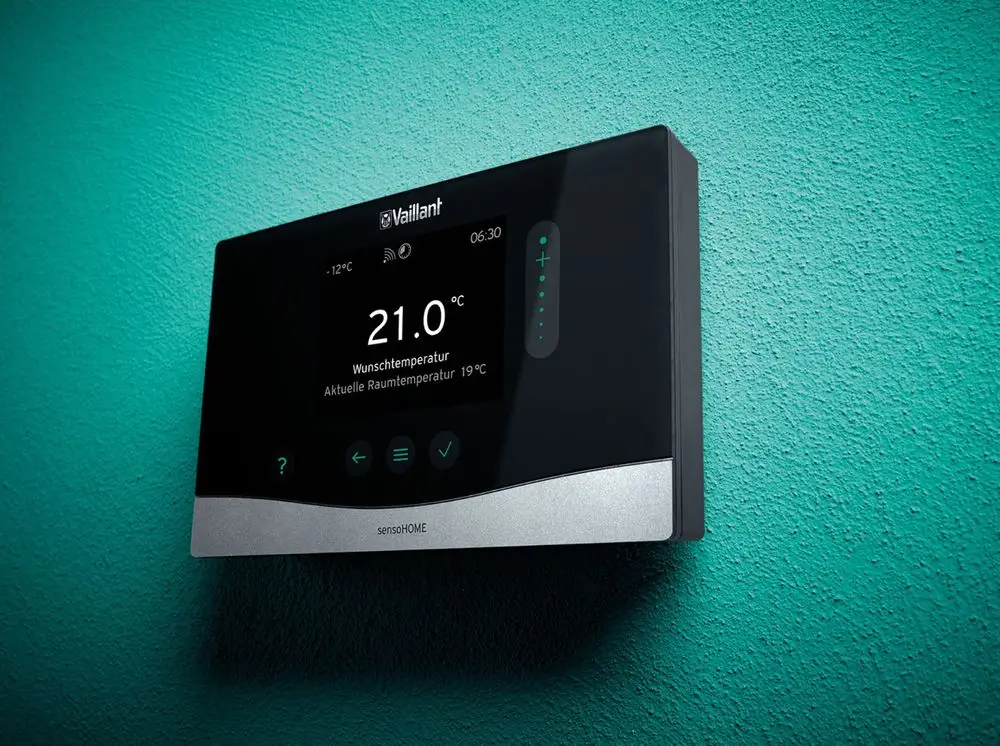 Vaillant Raumtemperaturregler mit digitalem Display, zeigt aktuelle und gewünschte Temperatur an, montiert an einer grünen Wand.
