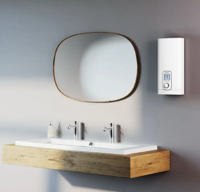 Weißer Durchlauferhitzer von Stiebel Eltron an einer Wand, neben einem modernen Waschbecken mit Holzablage und zwei Wasserhähnen, sowie einem ovalen Wandspiegel darüber.