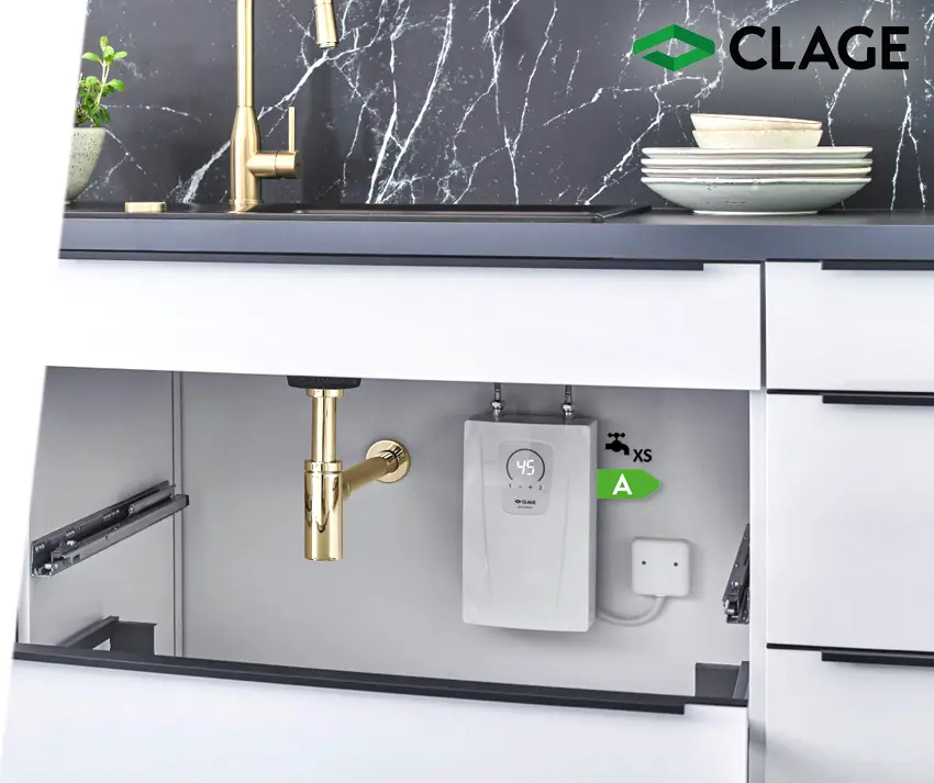 Weißer Heizgerät von CLAGE unter einer Küchenarbeitsplatte, verbunden mit Wasserleitungen, neben einer goldenen Armatur und Geschirr.