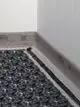 Schwarze Dämmstreifen mit Noppenstruktur und einer Umrandung aus transparentem Material, die an einer Wand platziert sind. Produkt von Kermi.