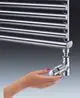 Thermostatventil von Oventrop mit dreifacher Skala und verchromter Oberfläche, Hand mit rotem Nagellack stellt Bedienung dar, Heizkörper im Hintergrund sichtbar.