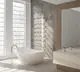 Weißer Badheizkörper von HM Heizkörper, vertikal montiert, an einer dekorativen Wand in einem modernen Badezimmer mit freistehender Badewanne und großen Fenstern.