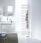Vertikaler weißer Zehnder-Heizkörper mit horizontalen Streifen vor einem minimalistischen Badezimmer mit einem Waschbecken und einem Spiegel. Eine braune Bademantel hängt daneben.