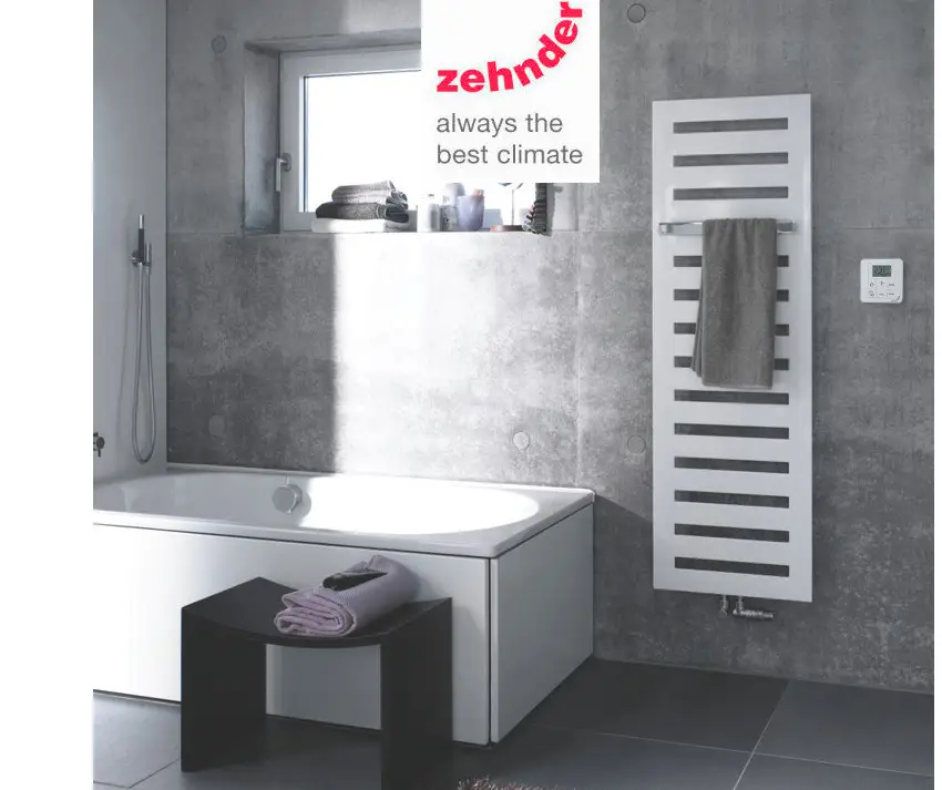 Vertikaler weißer Heizkörper von Zehnder mit Längsrippen und Handtuchhalter in modernem Badezimmer mit grauer Wand und Badewanne.