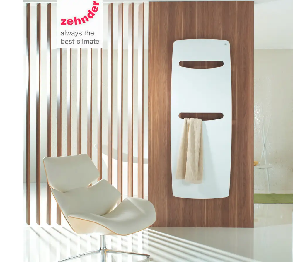 Vertikaler Zehnder Designheizkörper in Weiß mit Handtuchhalter, montiert an einer Holzverkleidung, vor einem modernen, hellen Raum.