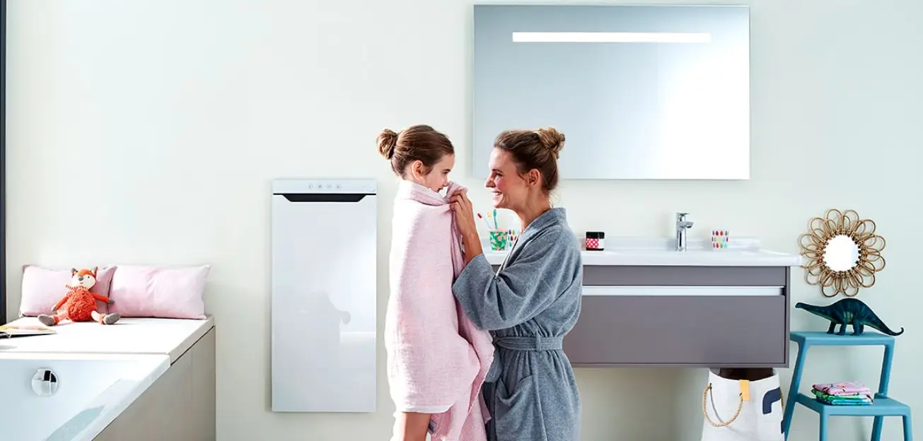 Zehnder Elektroheizkörper an der Wand in modernem Badezimmer, neben einem Waschbecken. Kinder und Erwachsene interagieren. Helle, klare Einrichtung mit Dekoration.