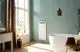 Zehnder Elektroheizkörper in weißer Farbe, flach und wandmontiert, neben ovaler Badewanne in modernem Badezimmer mit großen Fenstern und Holzfußboden.