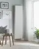 Purmo-Heizkörper, vertikal montiert und fein profiliert, steht an der Wand in einem hellen Raum, umgeben von einem Sofa, einem Tisch und Pflanzen.