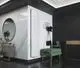 Vertikaler Heizkörper in Weiß, montiert an einer hellen Wand, neben einem Spiegel und einer modernen Garderobe. Marke Purmo sichtbar auf einer Tragetasche.
