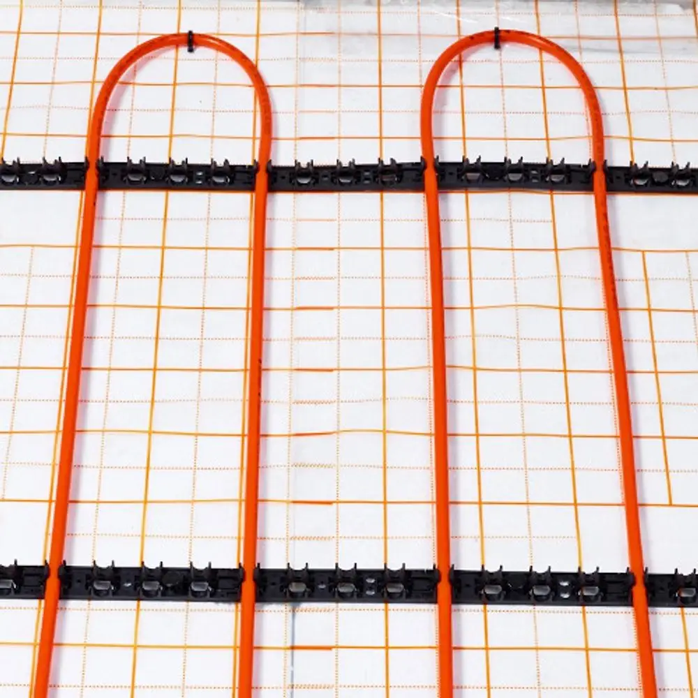 Orangefarbene Klemmschienen von Purmo, die zur Halterung von Heizungsrohren dienen, auf einem weißen Untergrund mit orangefarbenem Gittermuster.