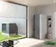 Kermi-Wärmepumpe in einem modernen Raum, neben einem Außenmodul. Die Pumpe hat eine graue Oberfläche und ist mit einem Regler ausgestattet. Offene Fenster mit Jalousien im Hintergrund.