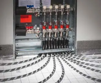 Kermi-Systemverteilereinheit mit mehreren Anschlussventilen und flexiblen Rohrleitungen auf dem Boden verlegt, zur Verteilung von Heizungs- oder Warmwassersystemen.