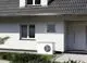 Weiße Außen Wärmepumpe von Stiebel Eltron, installiert neben einem Eingangsbereich, auf platingefliester Fläche vor einem modernen Wohnhaus.