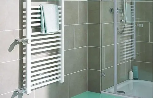 Weiße Handtuchheizung an einer gefliesten Wand im Badezimmer, mit einem hellblauen Handtuch und einer Duschkabine im Hintergrund.