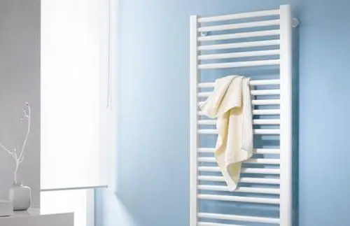 Weißer Badheizkörper mit horizontalen Lamellen, an dem ein beigefarbenes Handtuch hängt, vor einer blauen Wand in einem modernen Badezimmer.