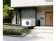Wärmepumpe von Stiebel Eltron an der Außenwand eines modernen Hauses, umgeben von einer gepflegten Rasenfläche und Pflanzen, mit Eingangstür und großen Fenstern im Hintergrund.