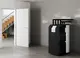 Stiebel Eltron Speicher-Hydraulikmodul in einem modernen Raum, auf einem grauen Boden, neben einer offenen Tür und einer Holztreppe, mit sichtbaren Rohren und einem Bedienfeld.
