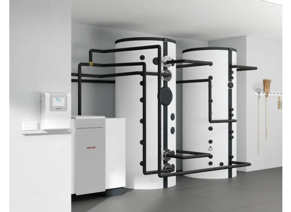 Zwei weiße Speichertanks mit schwarzen Rohrleitungen in einem modernen Raum. Ein Steuergerät von Stiebel Eltron ist an der Wand montiert.
