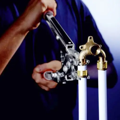 Ein Handwerker benutzt eine Rohrzange, um zwei Rohre mit goldenen Verbindungsstücken zu fixieren. Die Rohre sind weiß und scheinen zu einem plumbing System zu gehören.