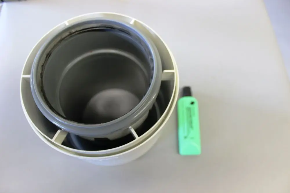 Graues Übergangsstück von Brötje, bestehend aus zwei runden Rohren, das ineinander gesteckt ist. Neben dem Produkt liegt ein hellgrüner Marker auf einer grauen Fläche.
