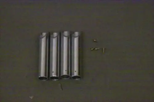 Vier metallische Rohre, die an einem Ende geöffnet sind, angeordnet in einer Reihe, daneben liegen mehrere kleine Schrauben. Produkt von Brötje.
