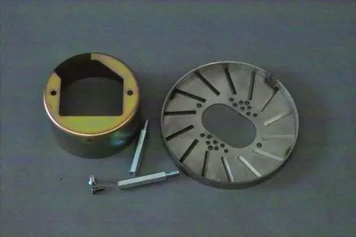 Zwei Metallteile, eines rund mit einer Öffnung, das andere flach und rund mit mehreren Löchern. Dazu vier Schrauben. Teile von Brötje, vermutlich für einen Gasanschluss.