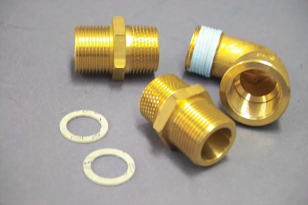 Brass fittings und Dichtungen von Brötje, darunter ein 90-Grad-Winkelstück und Verbindungselemente, auf grauem Hintergrund arrangiert.