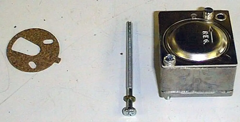 Erdgasregler von Brötje bestehend aus einem rechteckigen Metallgehäuse mit einer runden Abdeckung, Schraube und einem Dichtungsring neben dem Gerät.