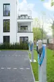 Zwei Mennekes-Ladestationen für Elektrofahrzeuge mit Kabeln, installiert auf einem gepflasterten Parkplatz neben einem modernen Wohngebäude und begrünten Bereichen.