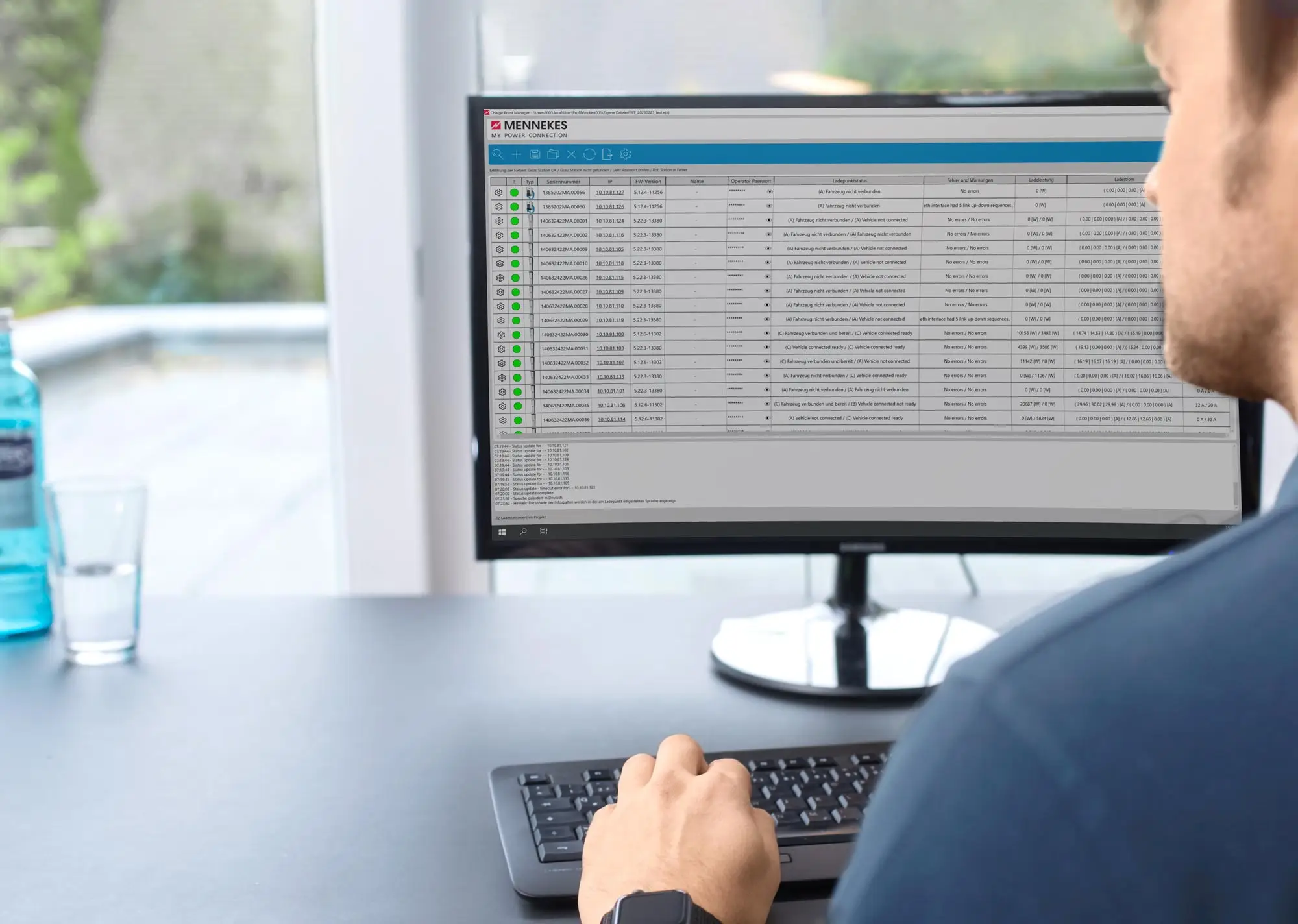 Bild eines Monitors mit einer Softwareanwendung zur Überwachung, in der Daten angezeigt werden. Auf dem Tisch stehen ein Glas Wasser und eine Flasche. Vor dem Monitor sitzt eine Person.