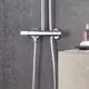 Grohe Duschsystem an der Wand montiert, bestehend aus einer Chrom-Duscharmatur und einem Schlauch, neben einer Seife und einem Parfüm auf einem Ablagetisch.
