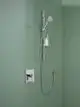 Brausearmatur von HANSA an einer grünen Wand, mit Halterung für Duschkopf und Ablage für Duschgel, sowie einem Bedienhebel zur Steuerung des Wasserflusses.