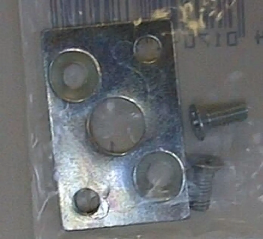 Metallplatte mit mehreren Löchern, zusammen mit zwei verschiedenen Schrauben, verpackt in einer transparenten Tüte, möglicherweise für Brötje-Produkte.