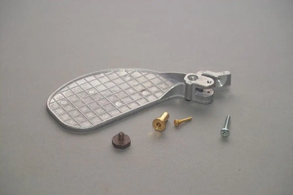 Brötje Luftklappe aus Metall mit Gitterstruktur, umgeben von verschiedenen Schrauben und Befestigungsstücken auf grauem Hintergrund.