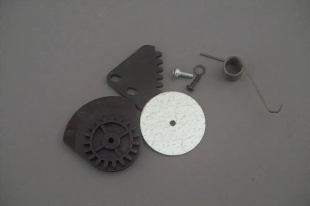 Brötje Stecksockel mit verschiedenen Einzelteilen, darunter Zahnräder, ein Metallring und Schrauben, auf grauem Hintergrund angeordnet.