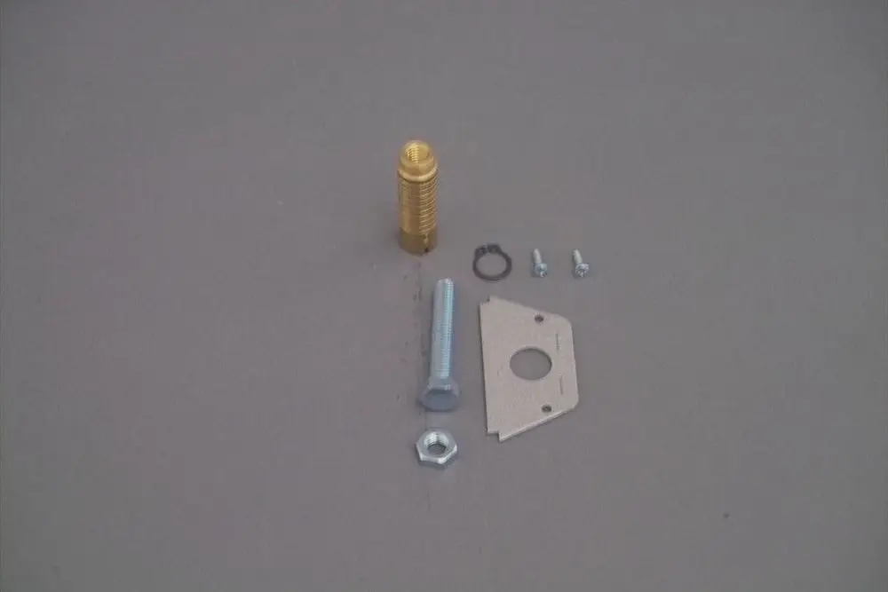 Brötje Druckregulierungsbauteile auf grauem Hintergrund, bestehend aus einer goldenen Verschraubung, Schrauben, einer Unterlegscheibe und einer Metallplatte.