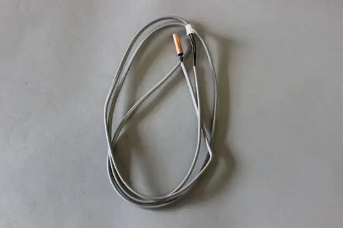 Graue, flexible Kabel mit zwei Anschlüssen, die einen Brötje Fühler bilden. Die Kabel sind schlank und verlaufen in einem leichten Bogen auf einem grauen Hintergrund.