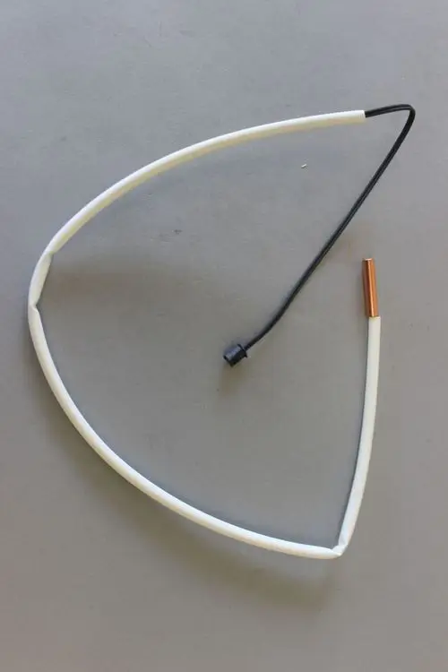 Brötje Fühler mit einer gebogenen weißen Umhüllung und einem schwarzen Kabel, das in eine kupferne Spitze übergeht, auf grauem Hintergrund.
