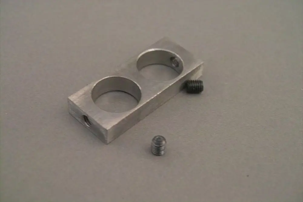 Brötje Arretierplatte aus Metall mit zwei runden Aussparungen, neben zwei kleinen Schrauben auf grauem Untergrund.