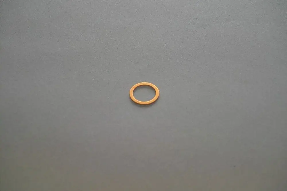 Kleine, runde Metalldichtung von Brötje in orangefarbenem Material auf grauem Hintergrund, mittig platziert.