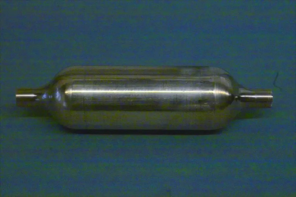Brötje Schalldämpfer aus Metall, zylindrische Form mit zwei Anschlussrohren an den Enden, auf einem einfarbigen Untergrund.