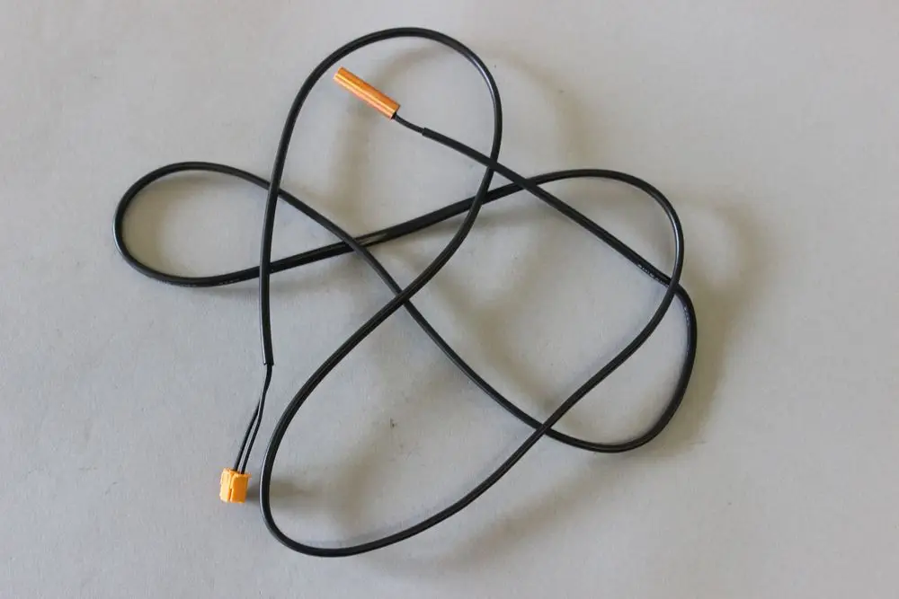 Schwarzes Kabel mit einem orangefarbenen Stecker, möglicherweise ein Temperatursensor oder Fühler von Brötje, auf einem grauen Hintergrund.