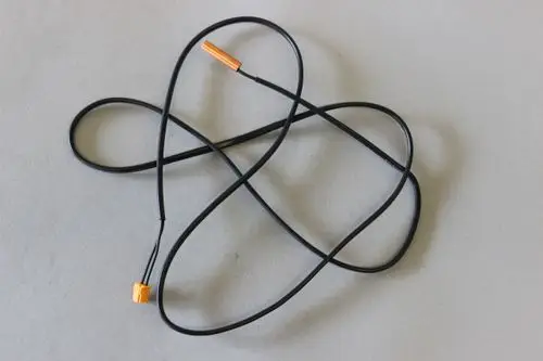 Schwarzes Kabel mit einem orangefarbenen Stecker, möglicherweise ein Temperatursensor oder Fühler von Brötje, auf einem grauen Hintergrund.